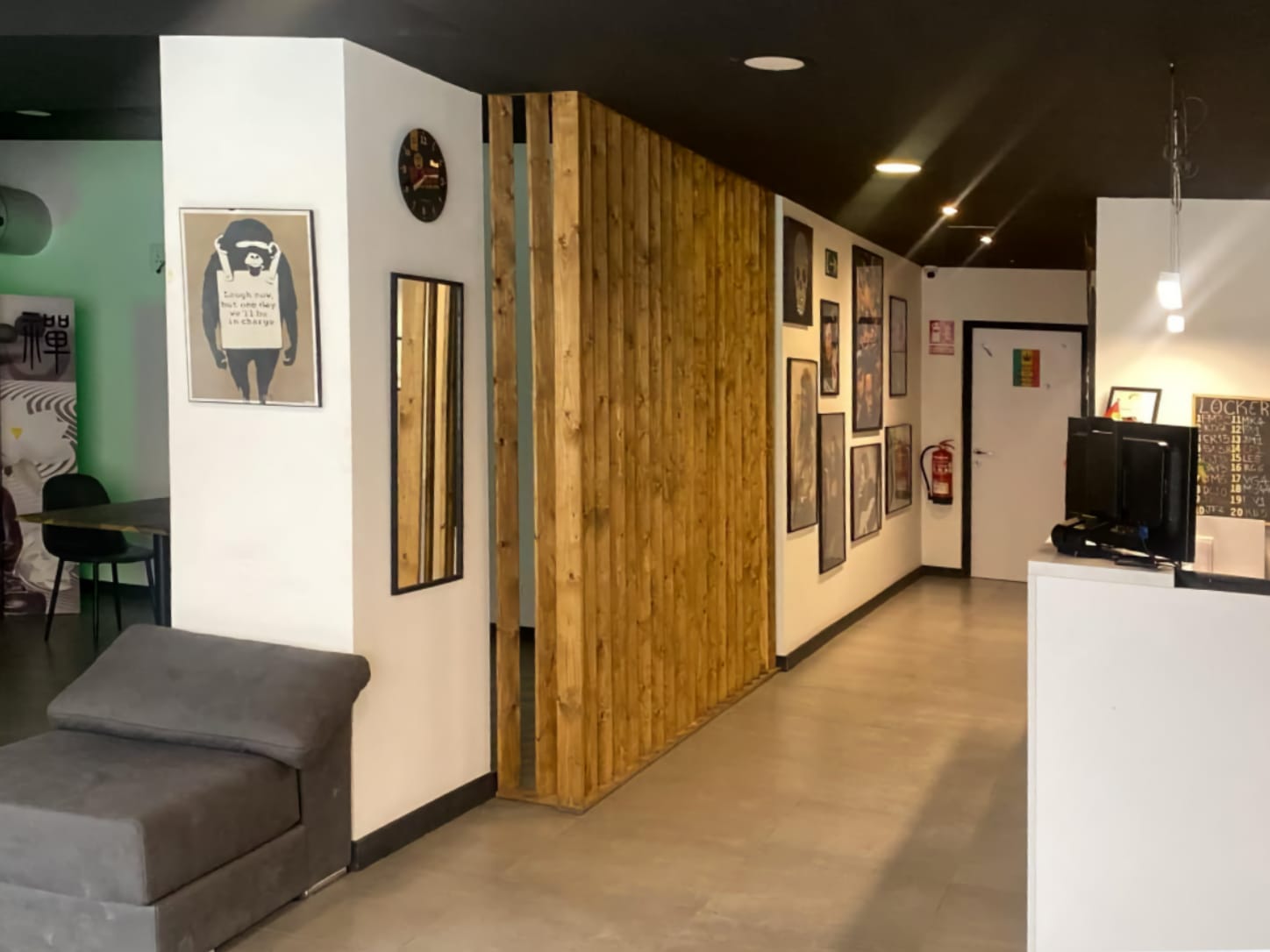 Il banco della reception e gli interni moderni del cannabis club Four Twenty di Valencia, con una parete divisoria in listelli di legno, quadri incorniciati e una poltrona grigia.