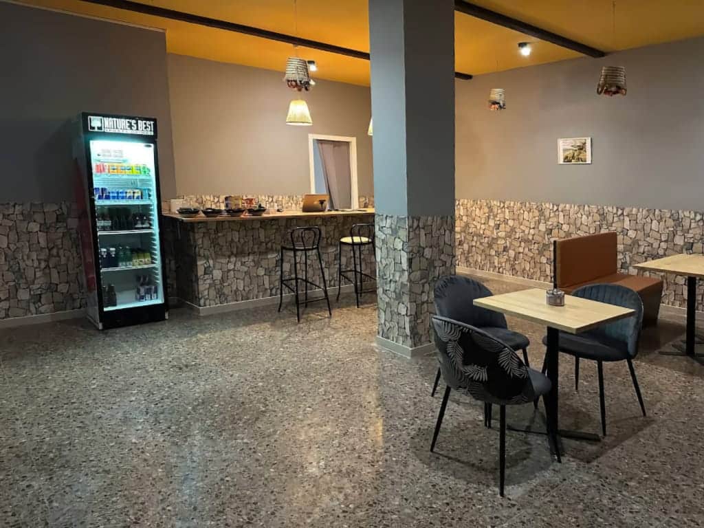 Interno del club di cannabis Magura a Valencia, con bancone in pietra, pavimento in terrazzo, sedute moderne e frigorifero per bevande.
