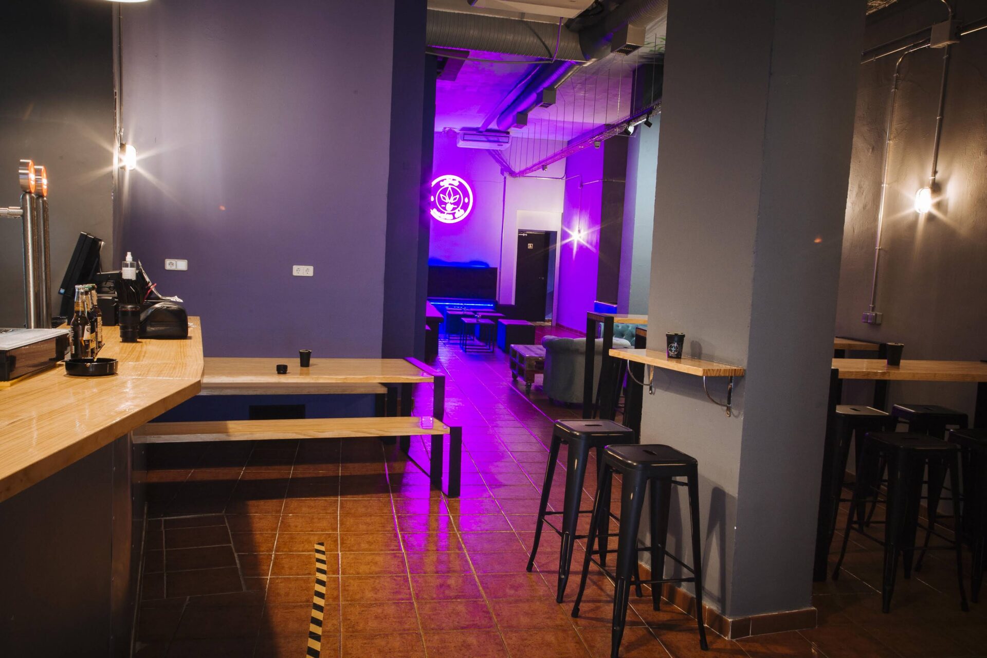 Zona bar e area con posti a sedere del club sociale della cannabis Enjoint a Madrid con luci al neon