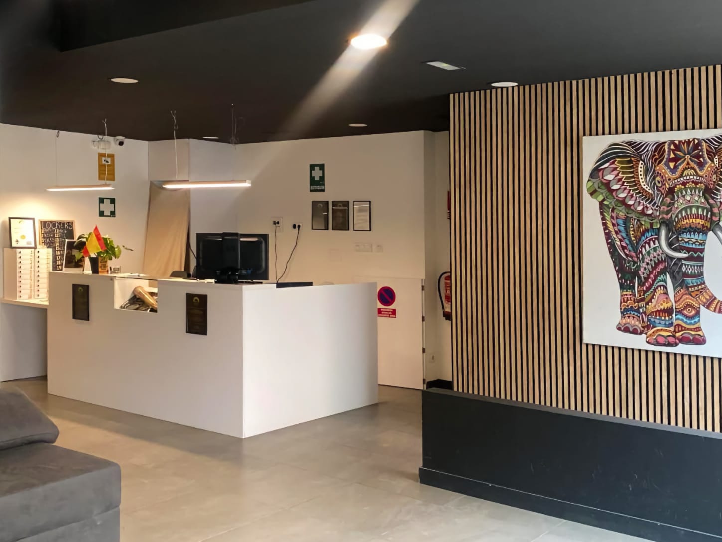 Il bancone della reception bianco e minimalista del cannabis club Four Twenty di Valencia, con illuminazione moderna e un dipinto colorato di un elefante su una parete in listelli di legno.