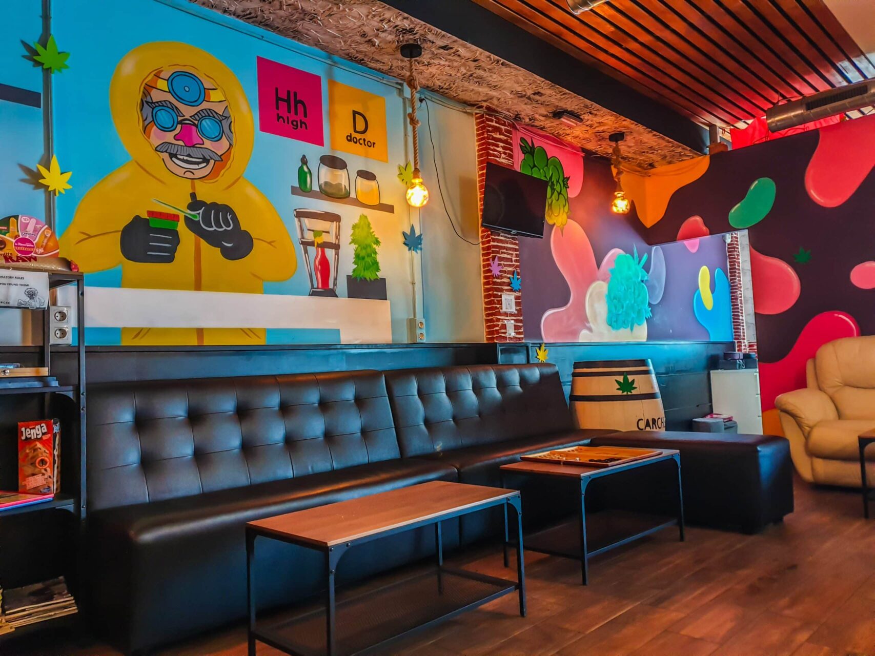 Interno del social club High Doctor ad Alicante con pareti graffiti colorate, divani pelle nera e pavimento legno.