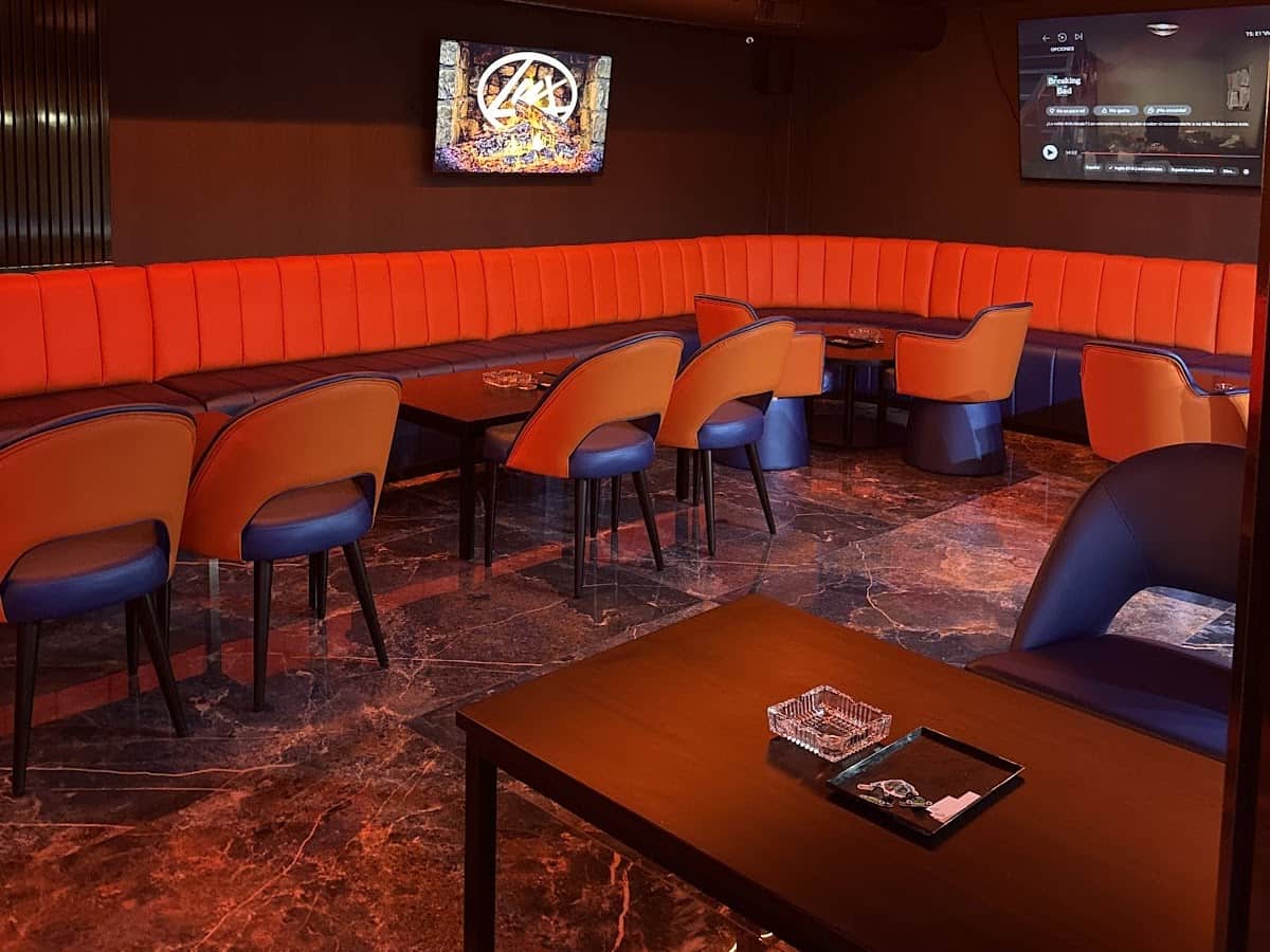 Interno del social club Lux Lounge a Marbella con divani velluto arancioni, schermo TV e pavimento marmo.