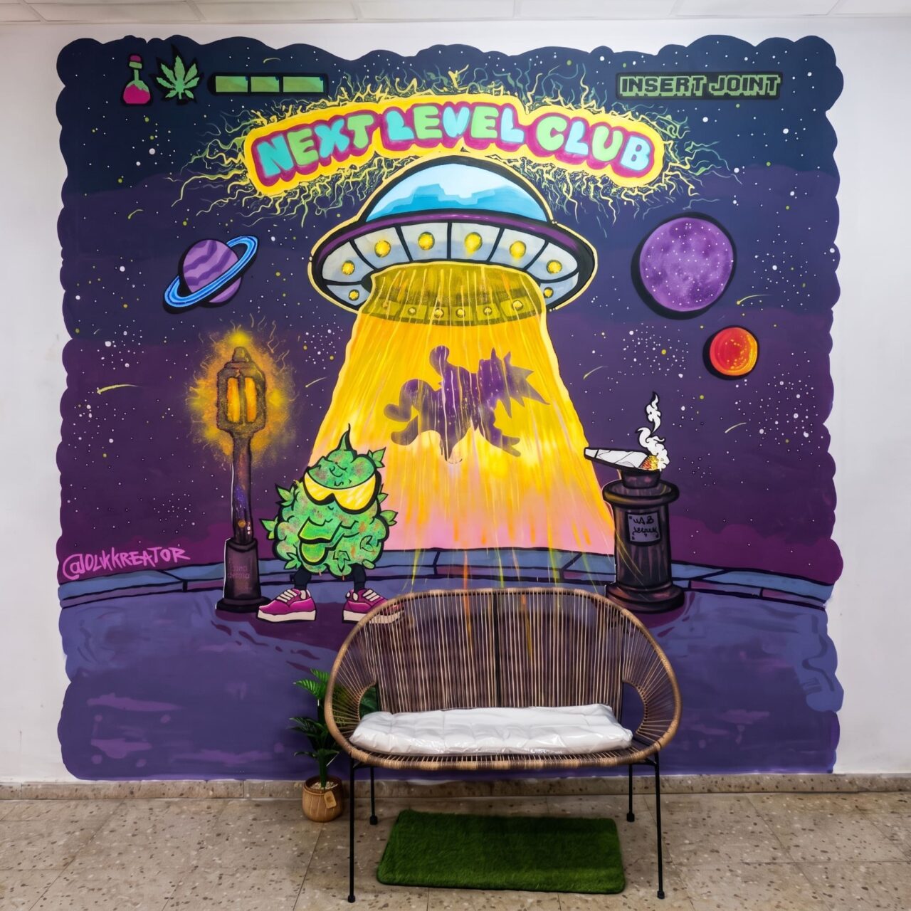 Interno del cannabis club Next Level Club a Valencia: una panca intrecciata davanti a un graffiti a tema UFO.