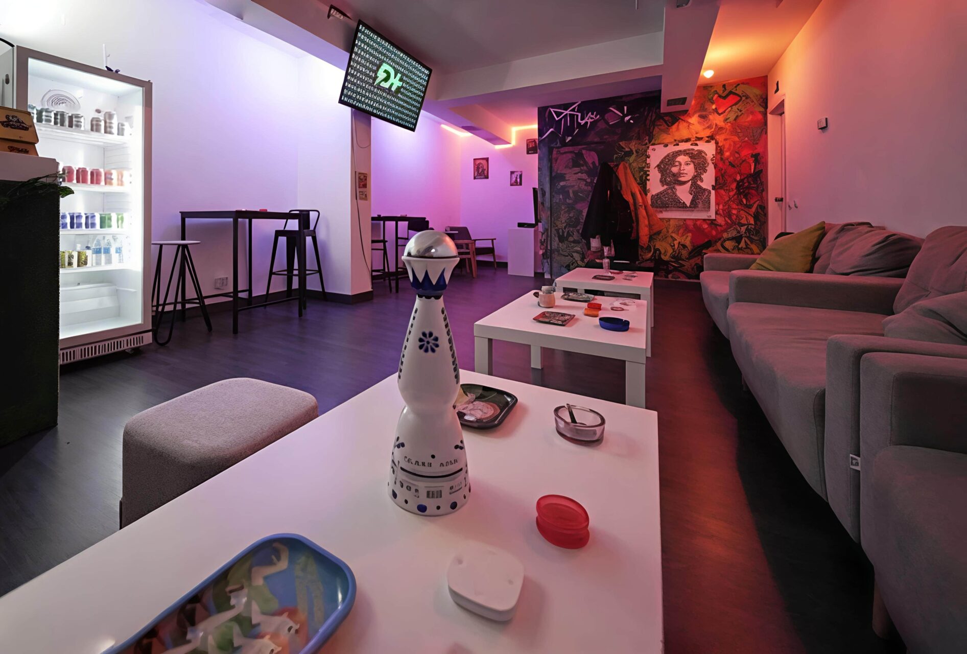 Area lounge nel Valhalla cannabis club a Madrid con illuminazione al neon blu e arancione, tavolini bassi e parete con graffiti.