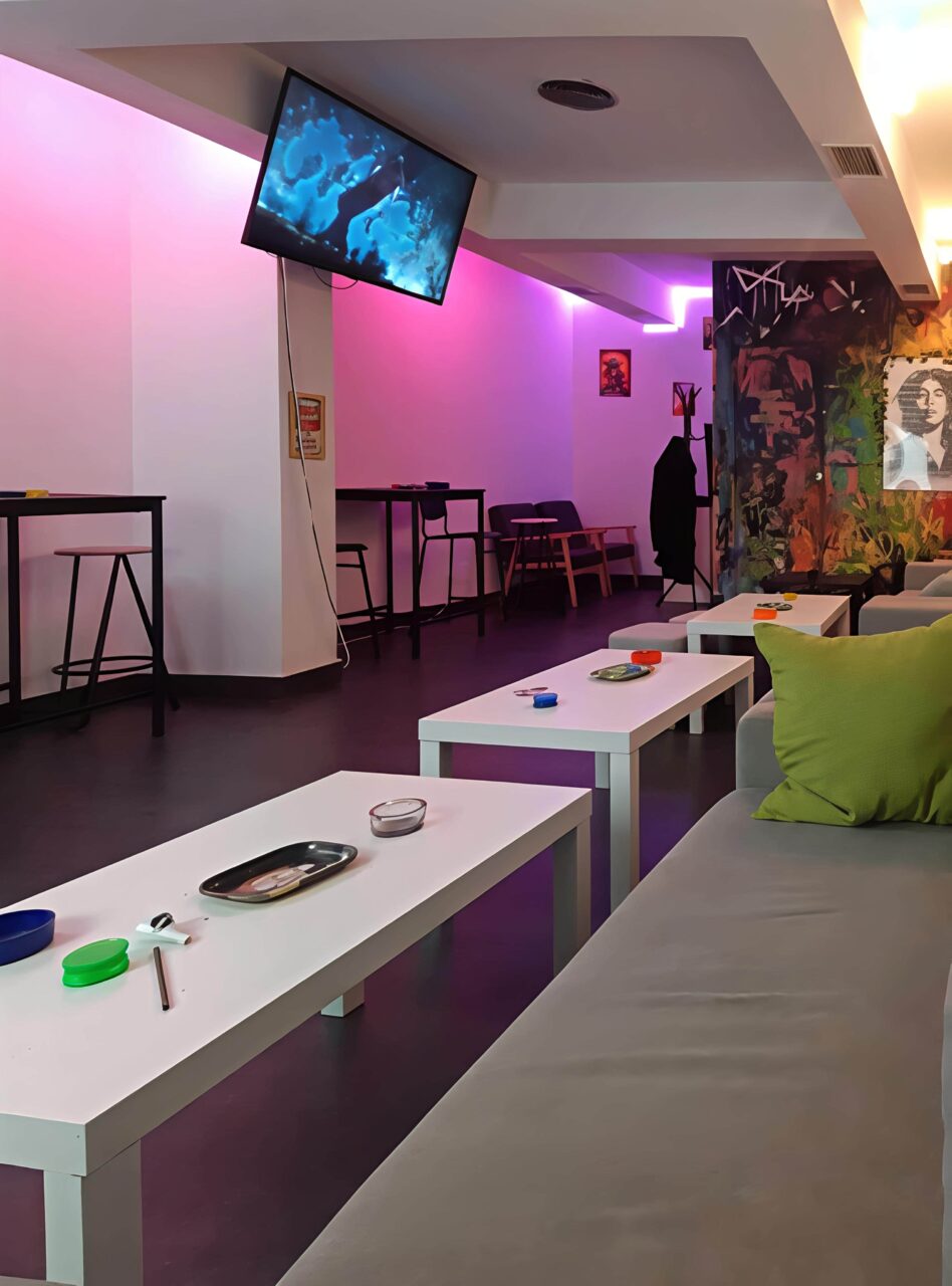 Interno moderno di una lounge con illuminazione al neon viola presso il Valhalla cannabis club a Madrid, con tavolini bassi, divani e sedie da bar.